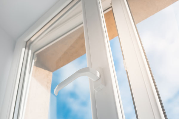 Vue détaillée d'une poignée de fenêtre blanche moderne ouverte, symbolisant des solutions d'isolation thermique et acoustique efficaces pour les maisons.